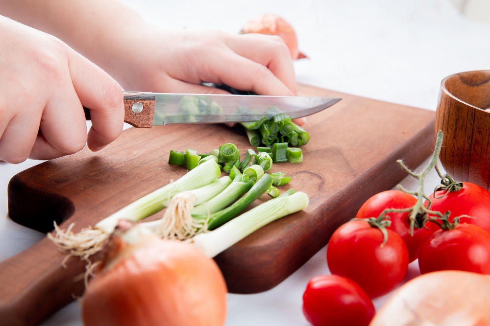 Close-up of a woman's hand cutting green onion on a cutting board with a knife